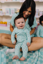 Woman holding a baby in matching teal outfits on a checkered blanket.