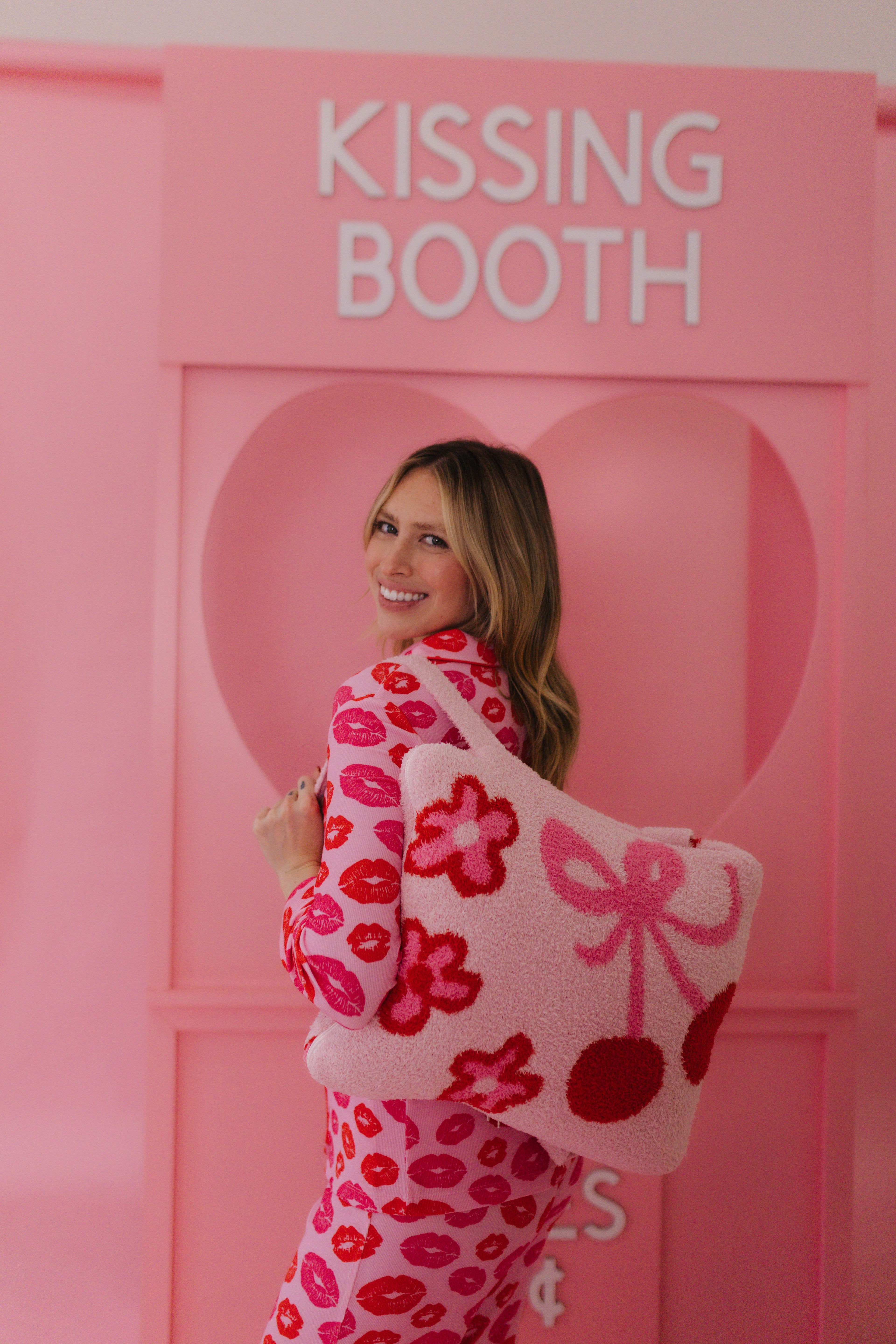 Woman in a pink and red outfit standing in front of a 'Kissing Booth' sign. showing the quillow on her back. 