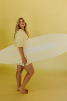 Woman holding a surfboard with 'STAYRATION' text on a yellow background