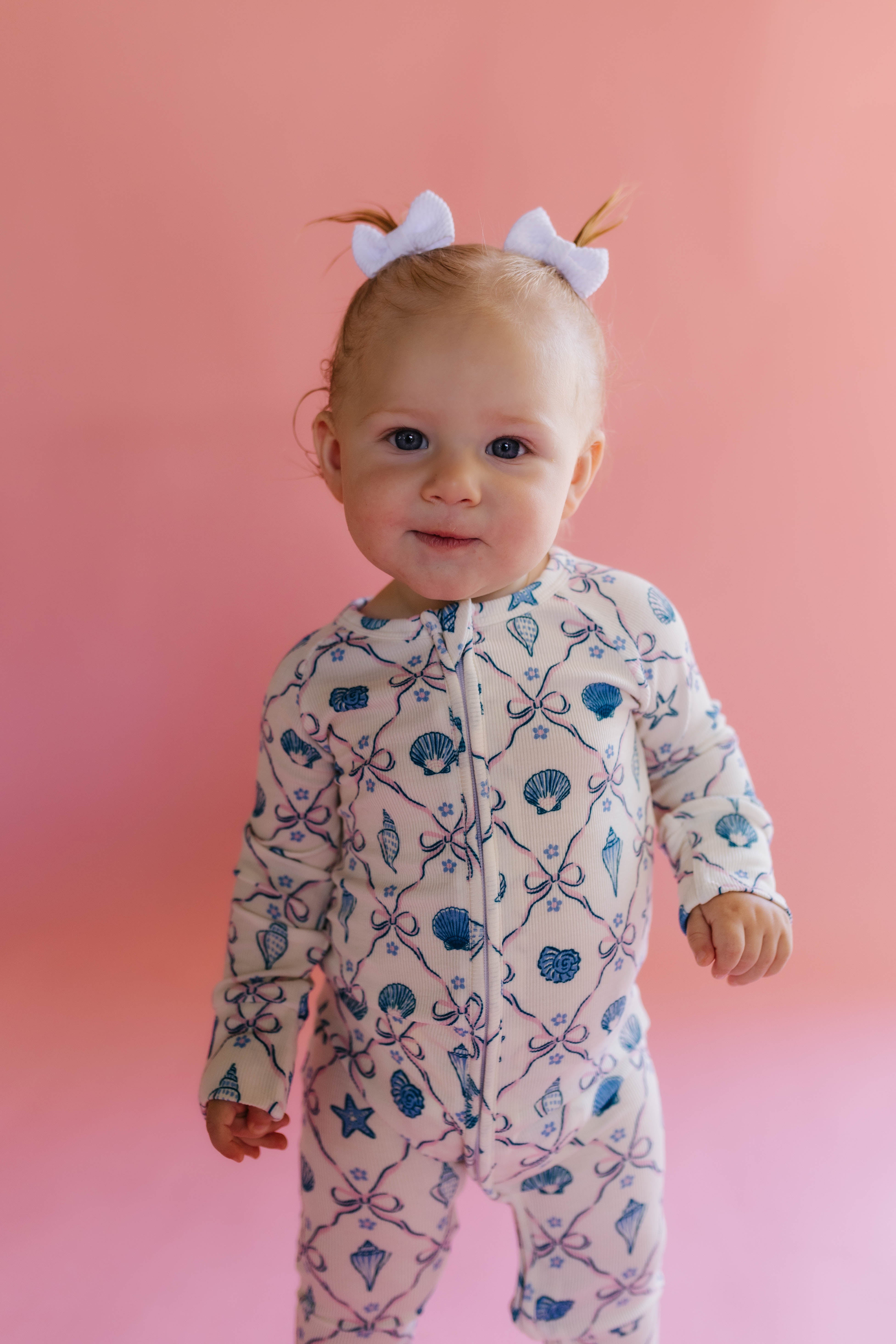 Baby wearing a patterned shell onesie against a pink background