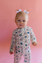 Baby wearing a patterned shell onesie against a pink background