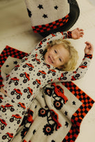 Child wearing a onesie with red and black patterns laying on the blanket