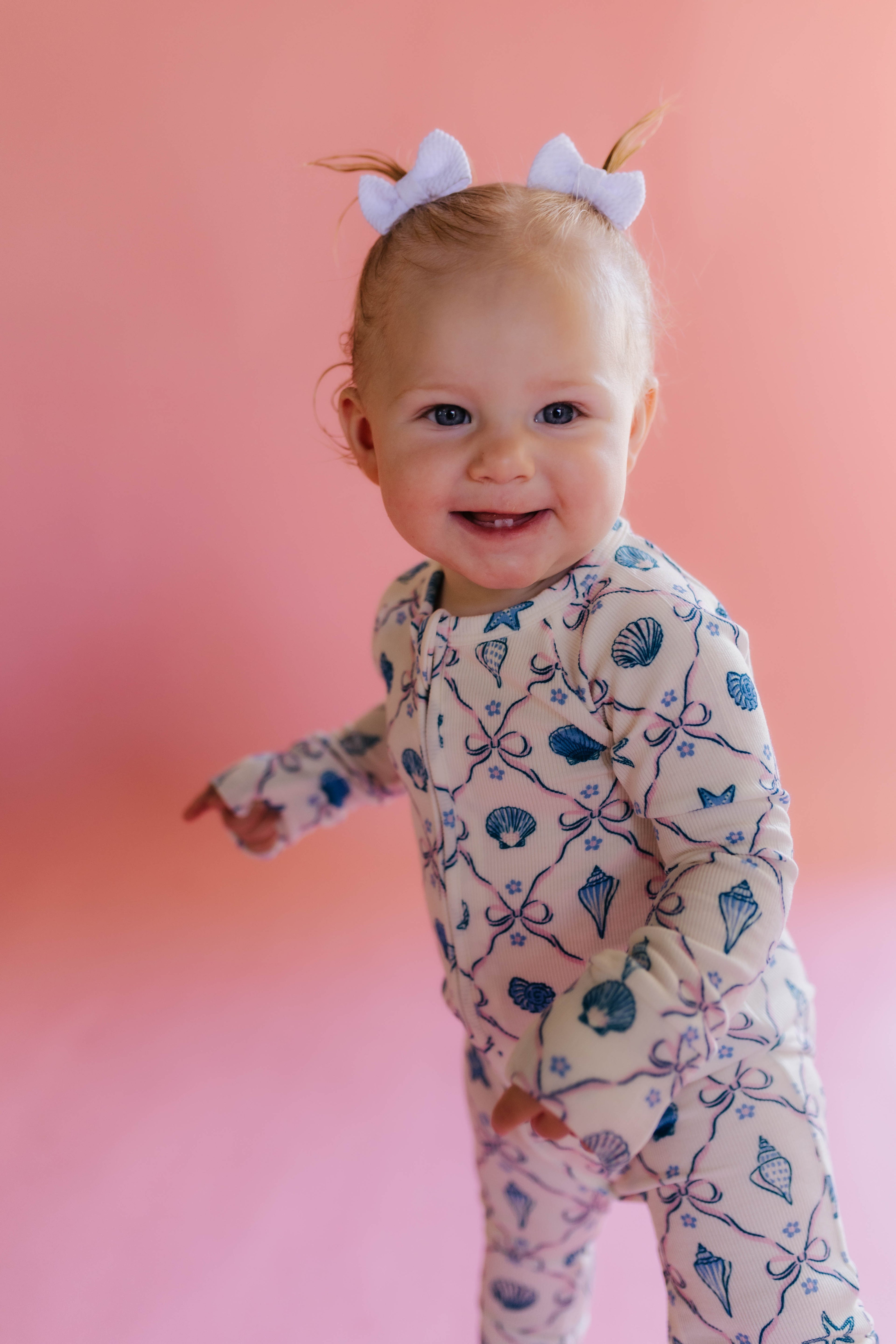 Baby wearing a patterned shell onesie on a pink background smiling