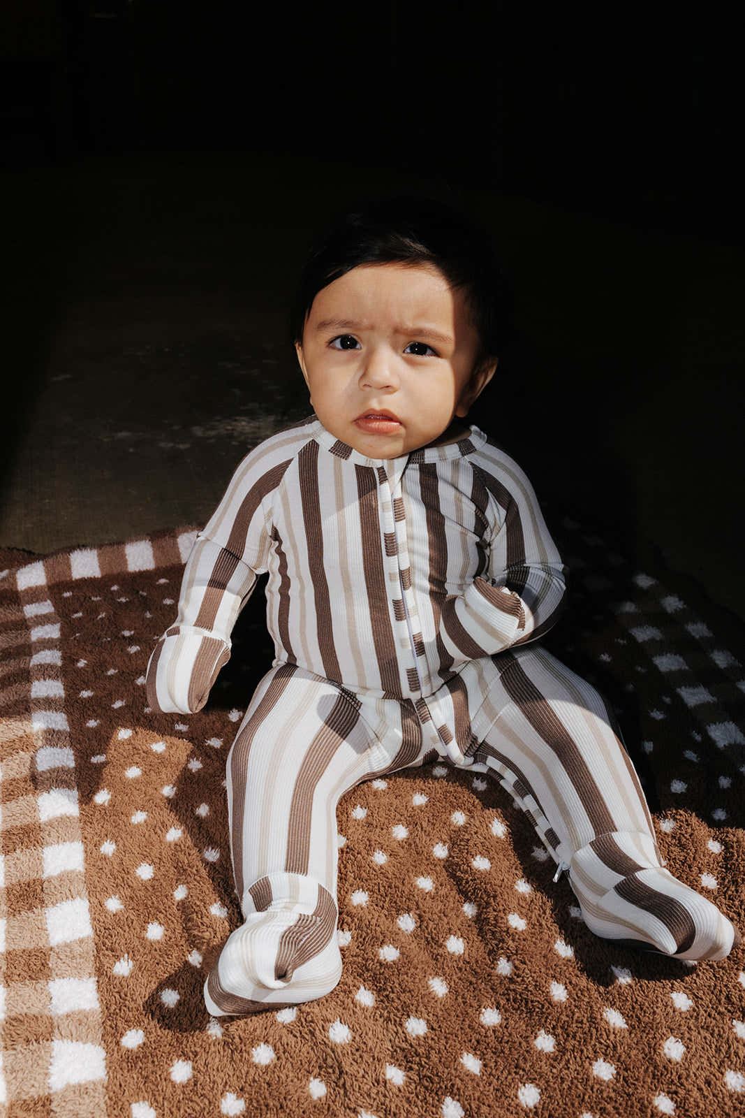 Baby wearing the brown and cream striped zip pajamas while seated on a brown blanket.