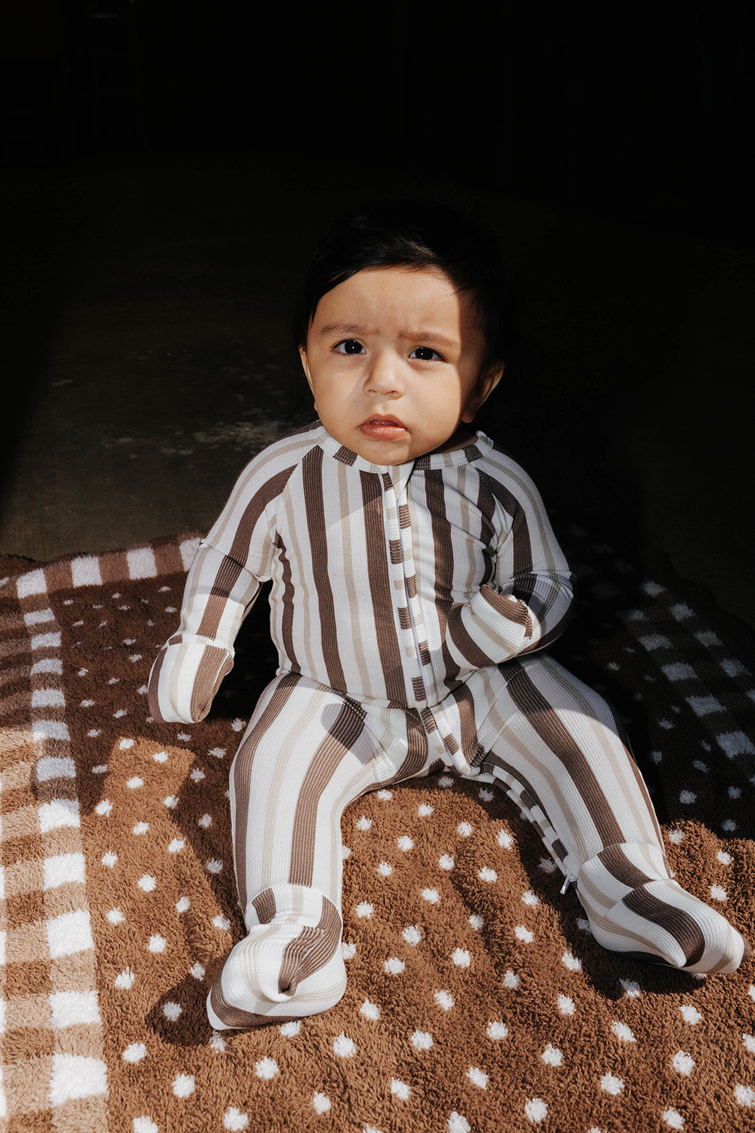 Baby wearing the brown and cream striped zip pajamas while seated on a brown blanket.