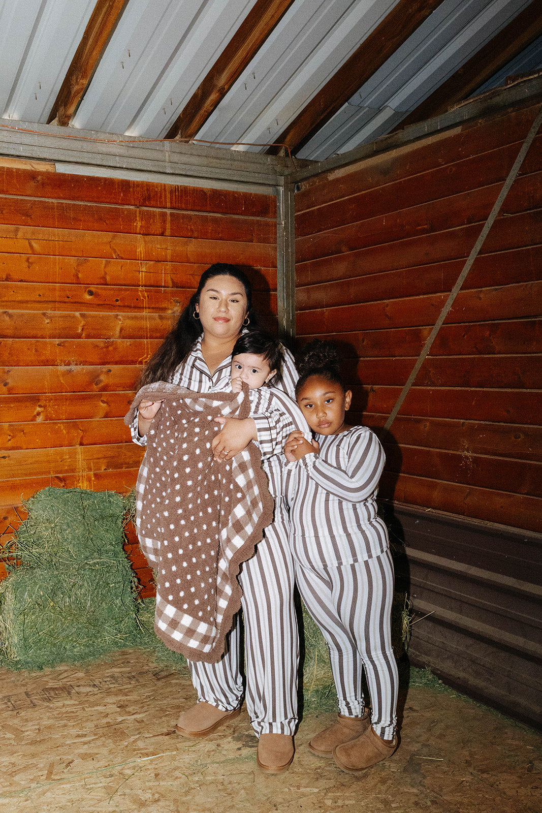 Adult and children wearing brown stripe pajamas and holding a gingham and polka dot kid blanket.