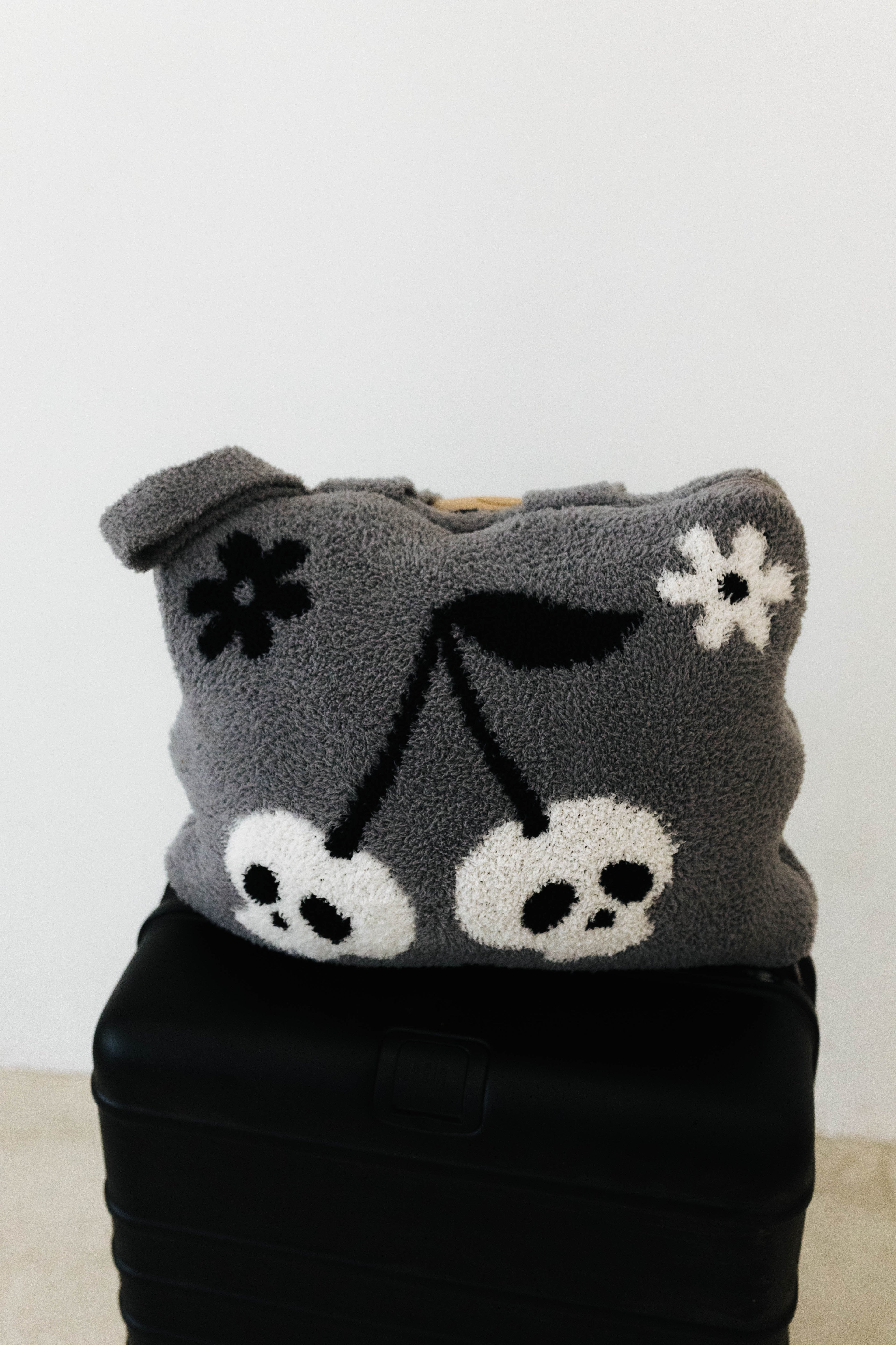skelly backpack/wristlet quillow on top of black suitcase