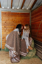 Brown gingham blanket draped over hay bales, showing the polka dot side and check border.