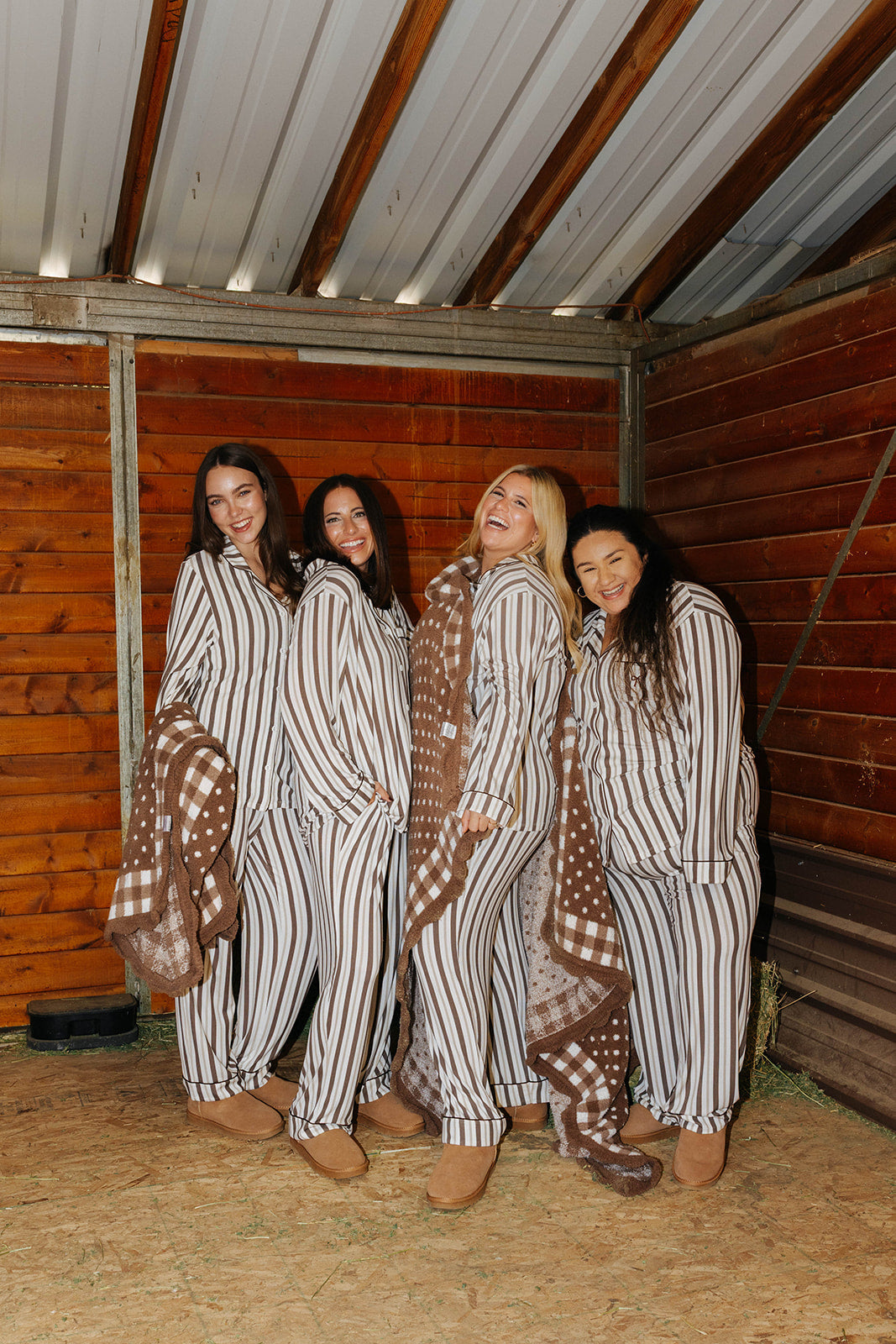 Models in striped pajamas holding the brown gingham blanket with polka dot reverse in a stable.