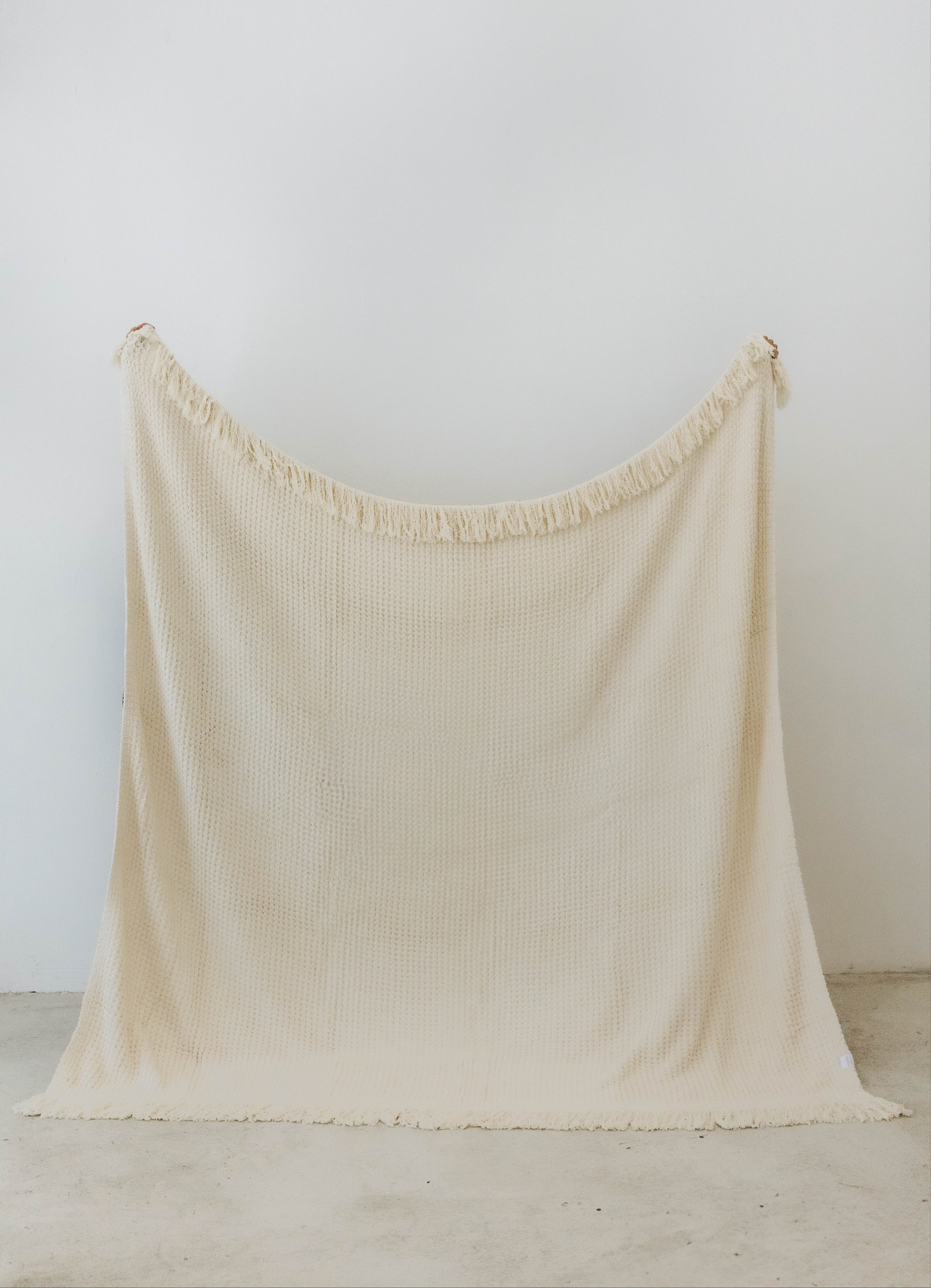 holding up cream waffle fringe blanket showing the size of the blanket 
