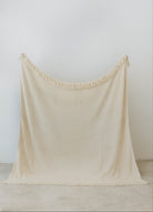 holding up cream waffle fringe blanket showing the size of the blanket 