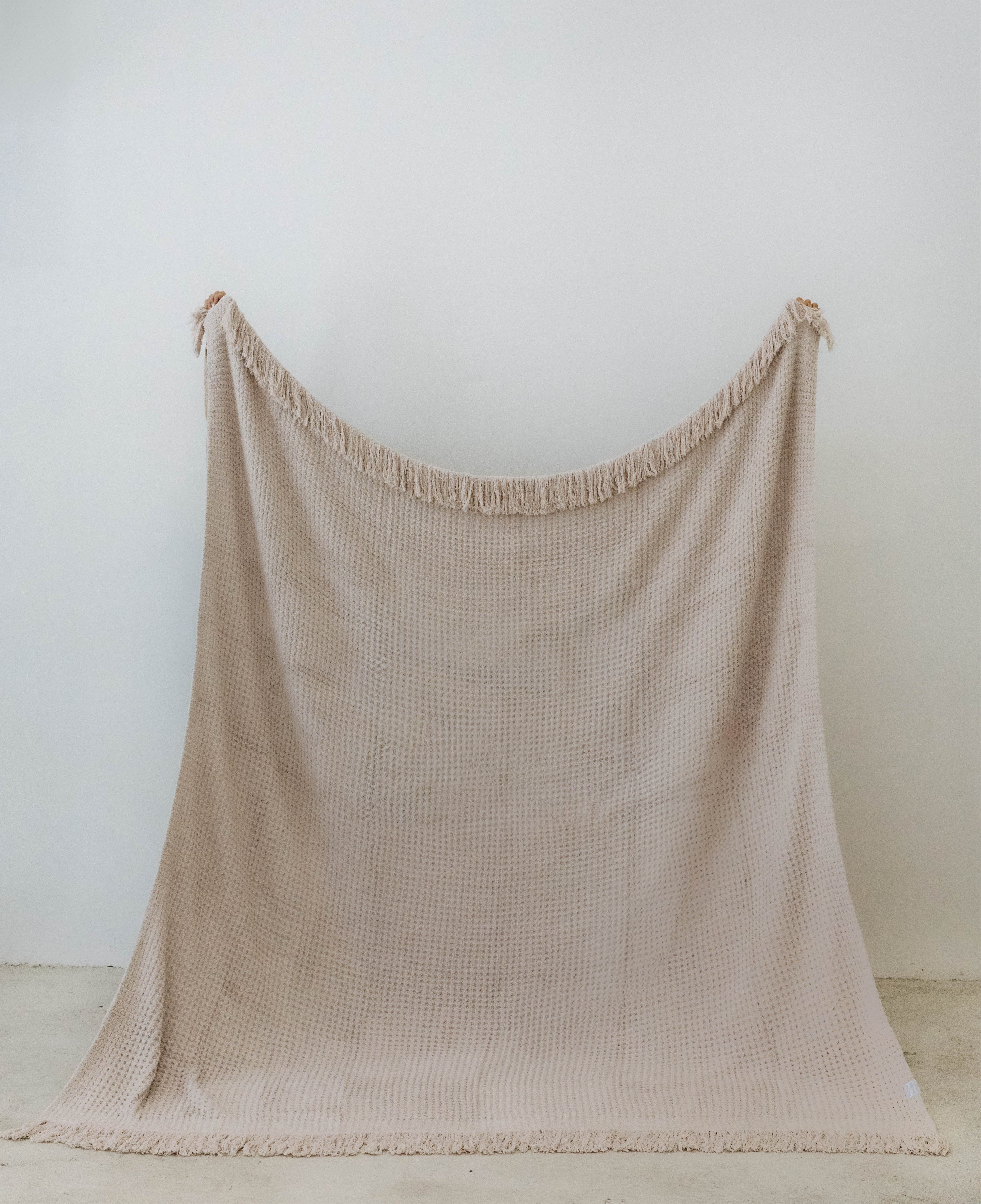 holding up the sand waffle fringe blanket showing the size of it 