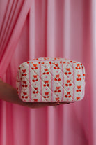 Quilted fabric pouch with red bow and cherrt pattern held against a pink curtain