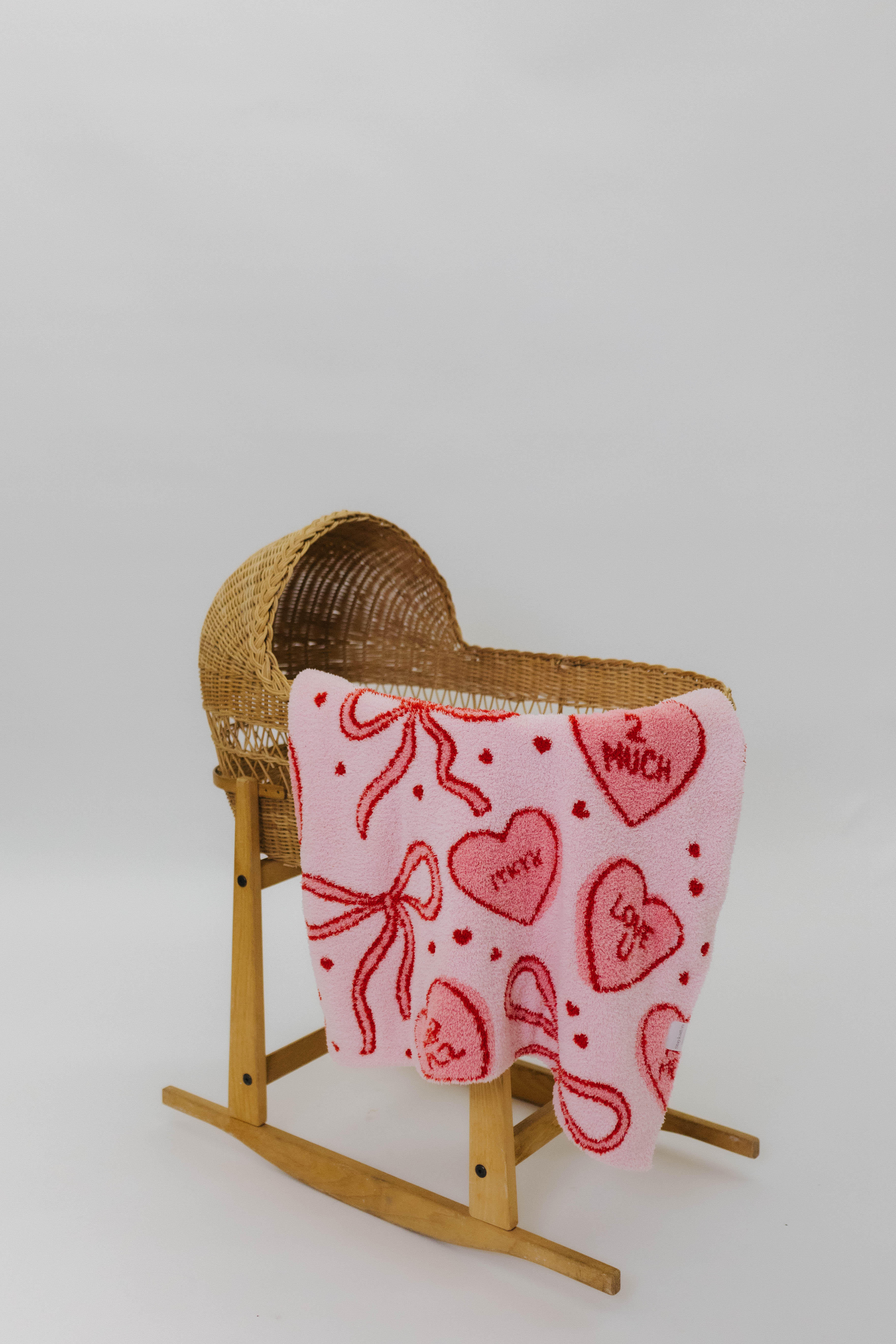 Wicker baby bassinet with pink blanket featuring red hearts and text on a white background