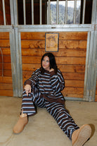 Model seated by a stable door wearing the striped sweatshirt and sweatpants.
