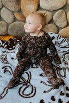 Side view of a baby wearing brown bow print zip pajamas on a matching bow quillow.