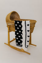 Wicker baby crib with a black and white heart-patterned blanket on a plain background