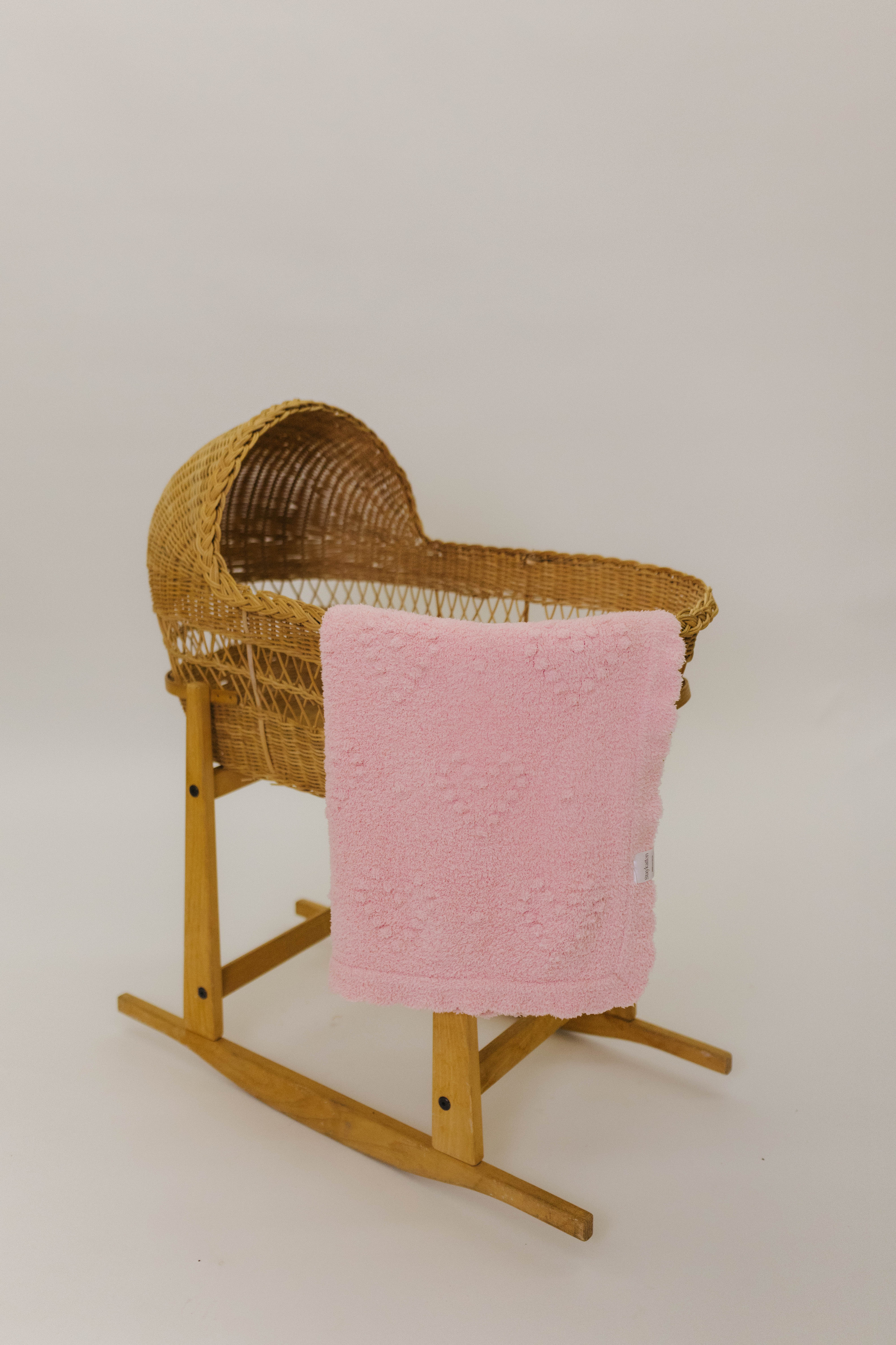 Wicker baby crib with a pink blanket on a white background
