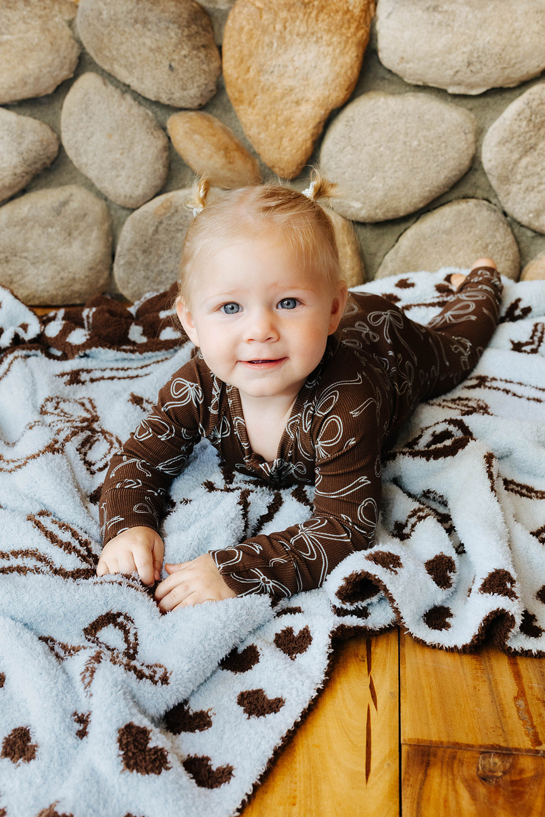 Baby in brown bow print zip pajamas on a blanket.