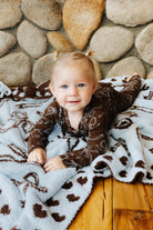 Baby in brown bow print zip pajamas on a blanket.