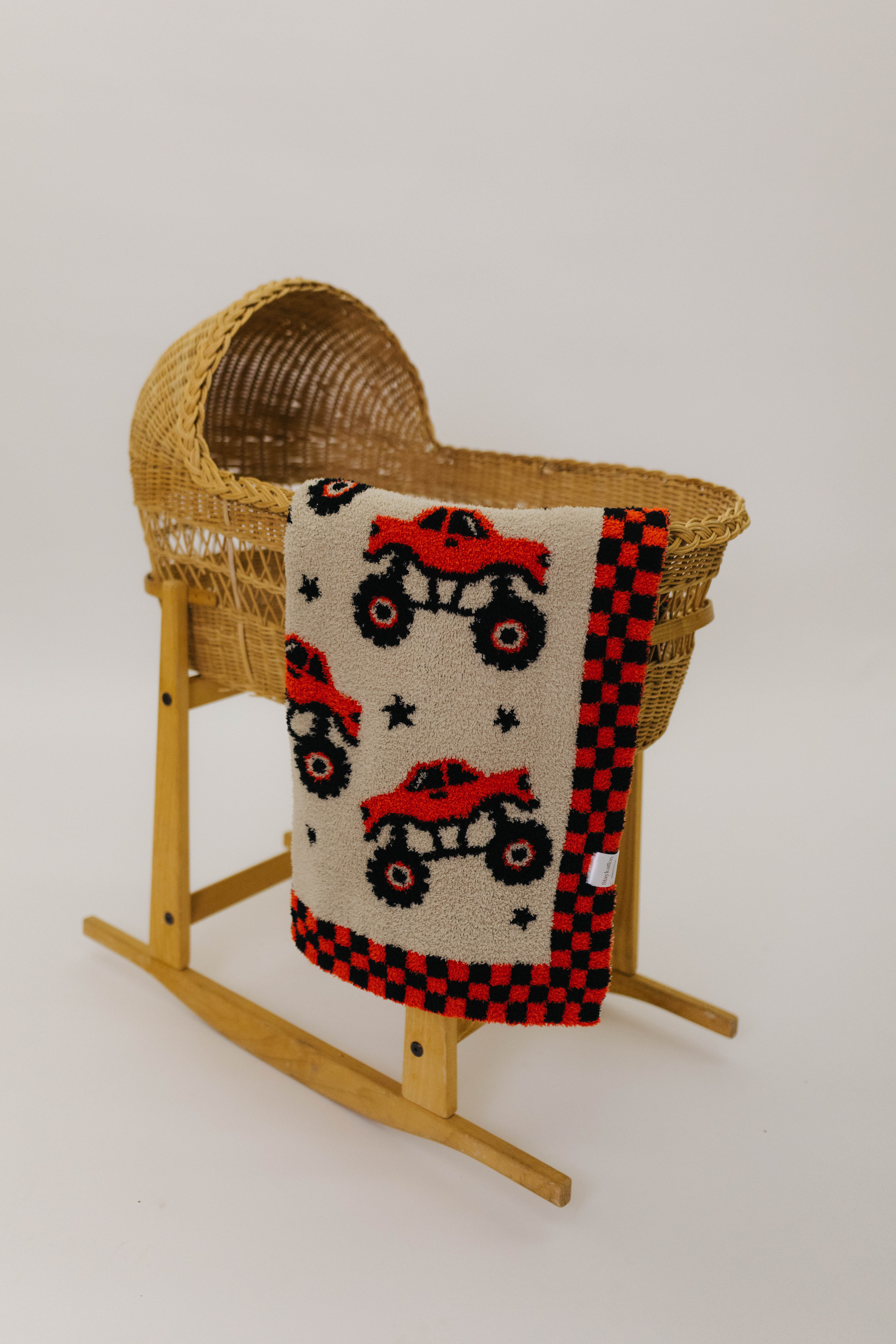 Wooden basket with a baby blanket featuring red monster trucks on a white background