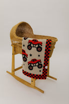 Wooden basket with a baby blanket featuring red monster trucks on a white background