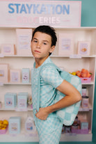 Young boy in a light blue checkered outfit with a quillow on his back
