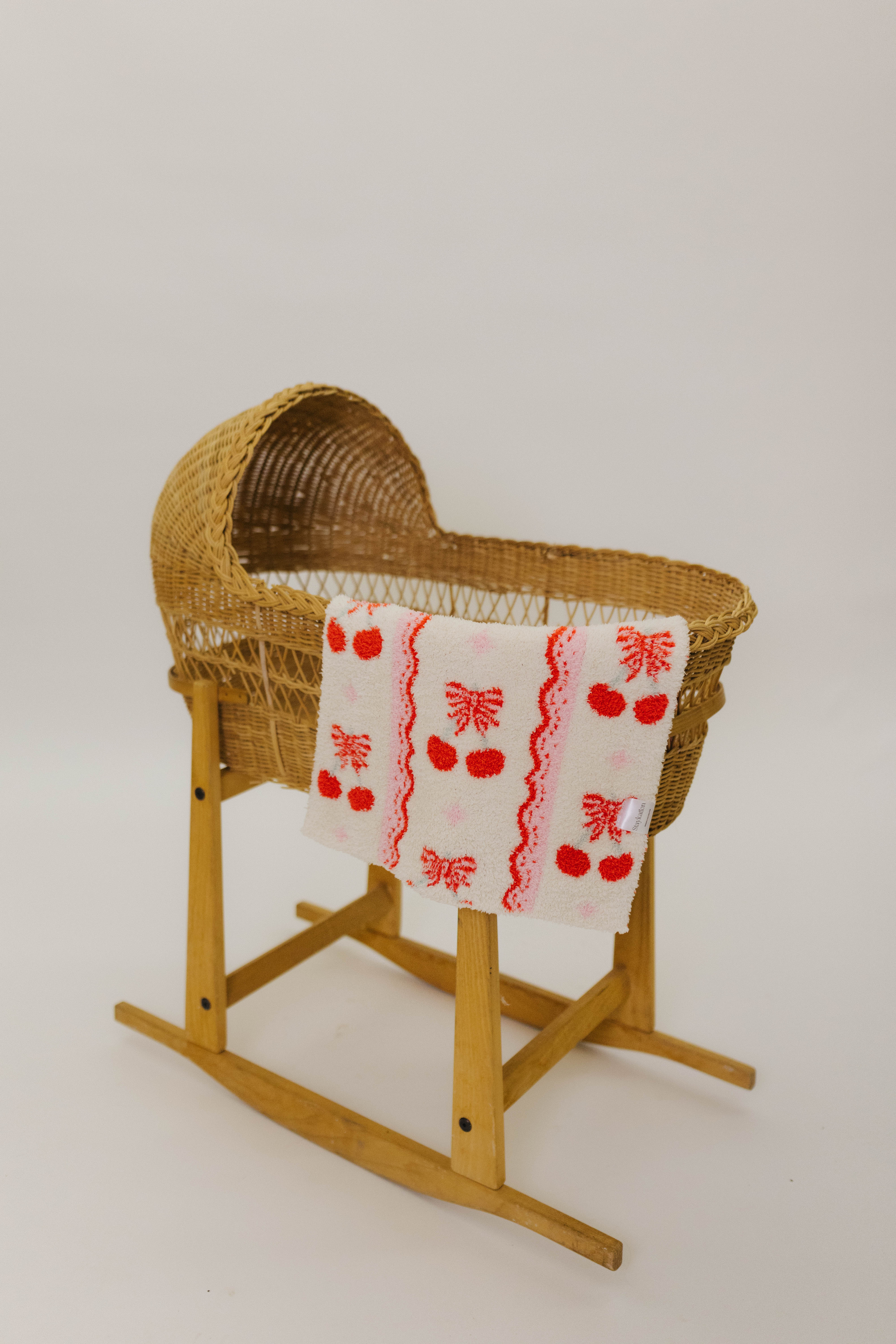 Wicker baby bassinet with a red and white patterned cherry blanket on a white background