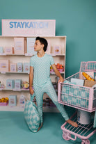 Person in teal pajama set with a shopping cart in a store setting, with 'STAYKATION' branding.