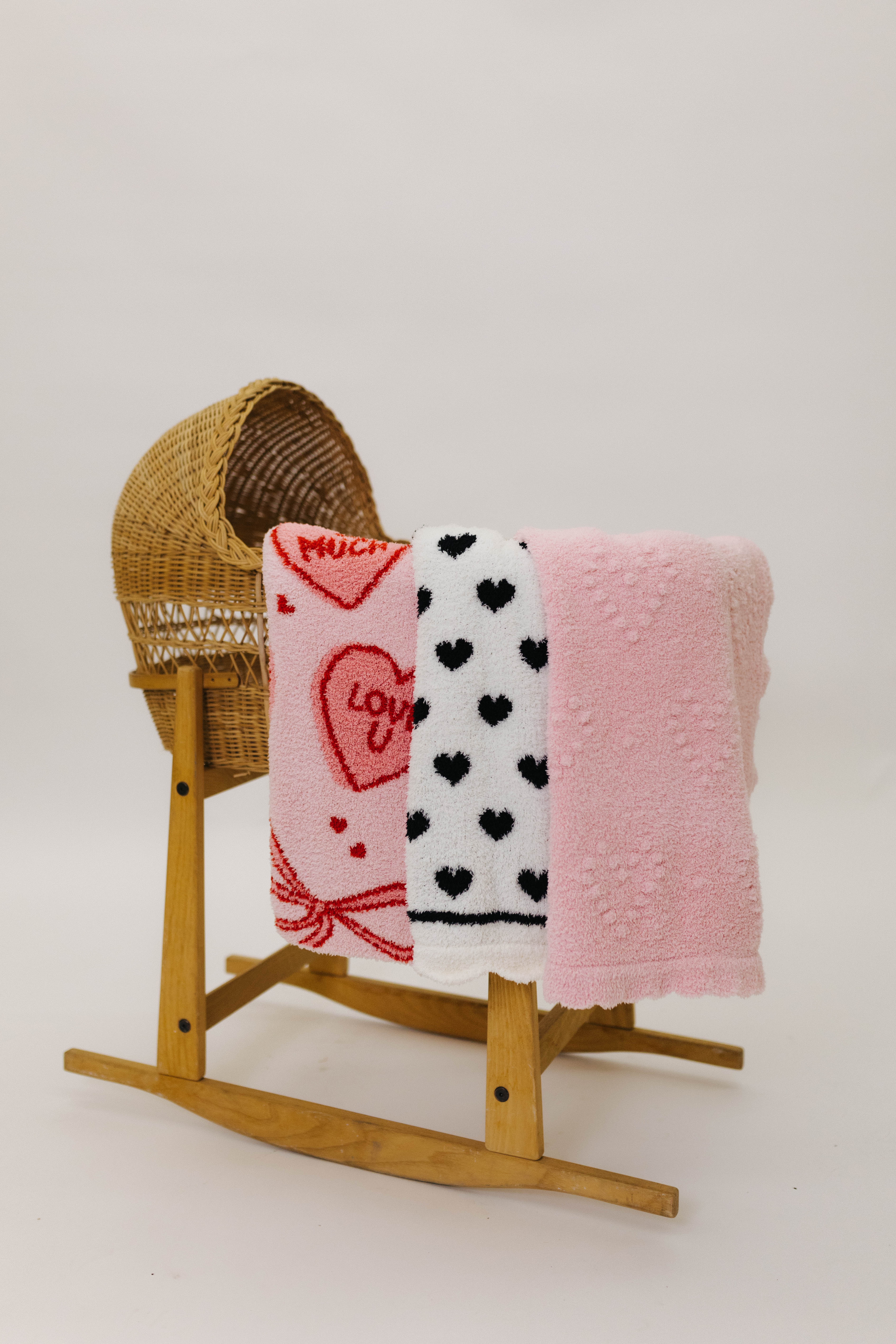 Blanket with heart patterns draped over a wooden rocking chair on a white background