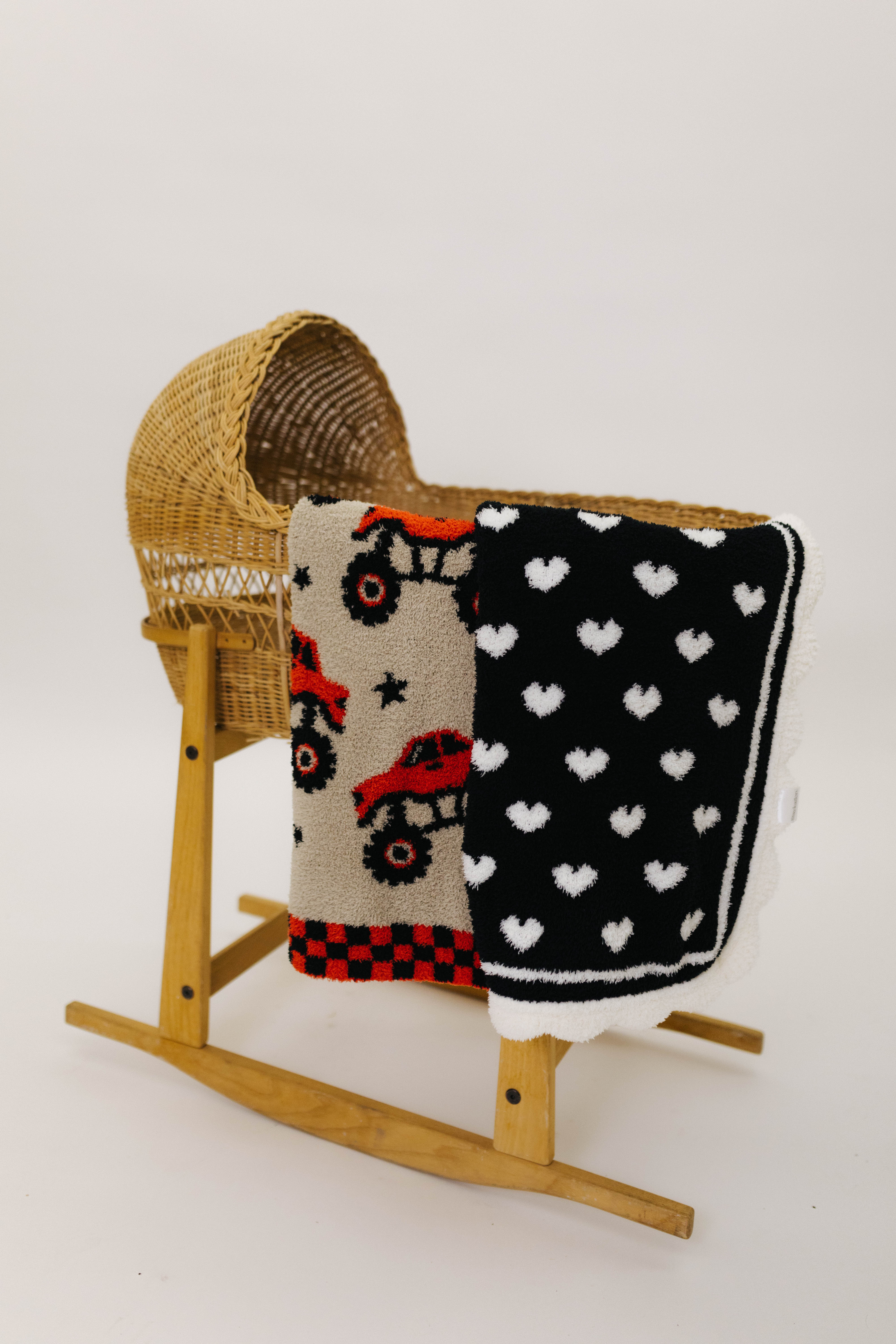 Wooden rocking chair with a baby blanket featuring monster trucks and another with heart patterns on a white background.