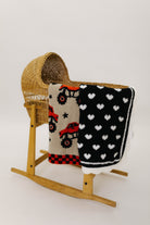 Wooden rocking chair with a baby blanket featuring monster trucks and another with heart patterns on a white background.