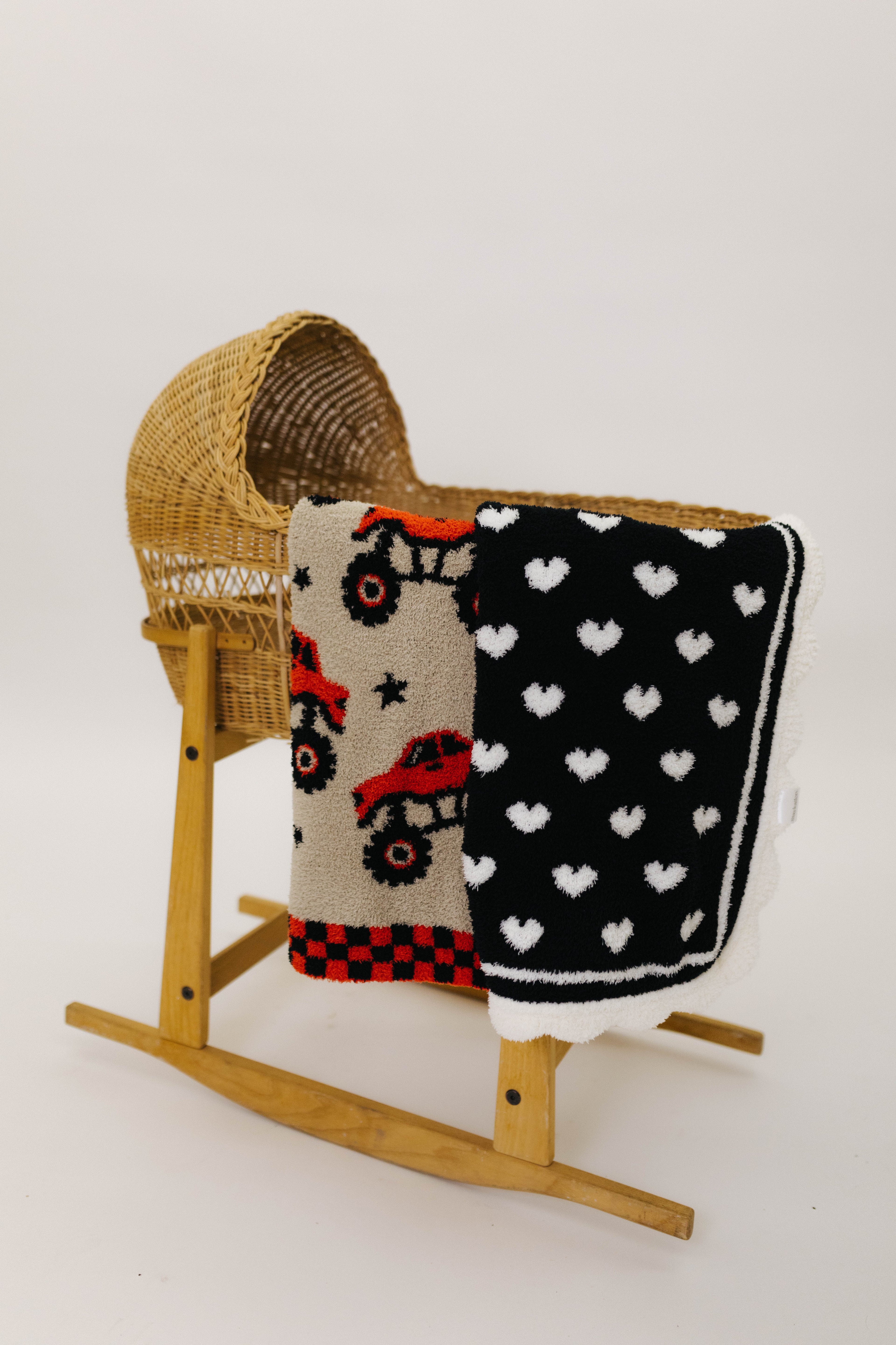 Wooden rocking chair with a baby blanket featuring monster trucks and another with heart patterns on a white background.