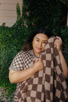 Model holding up the brown check blanket.