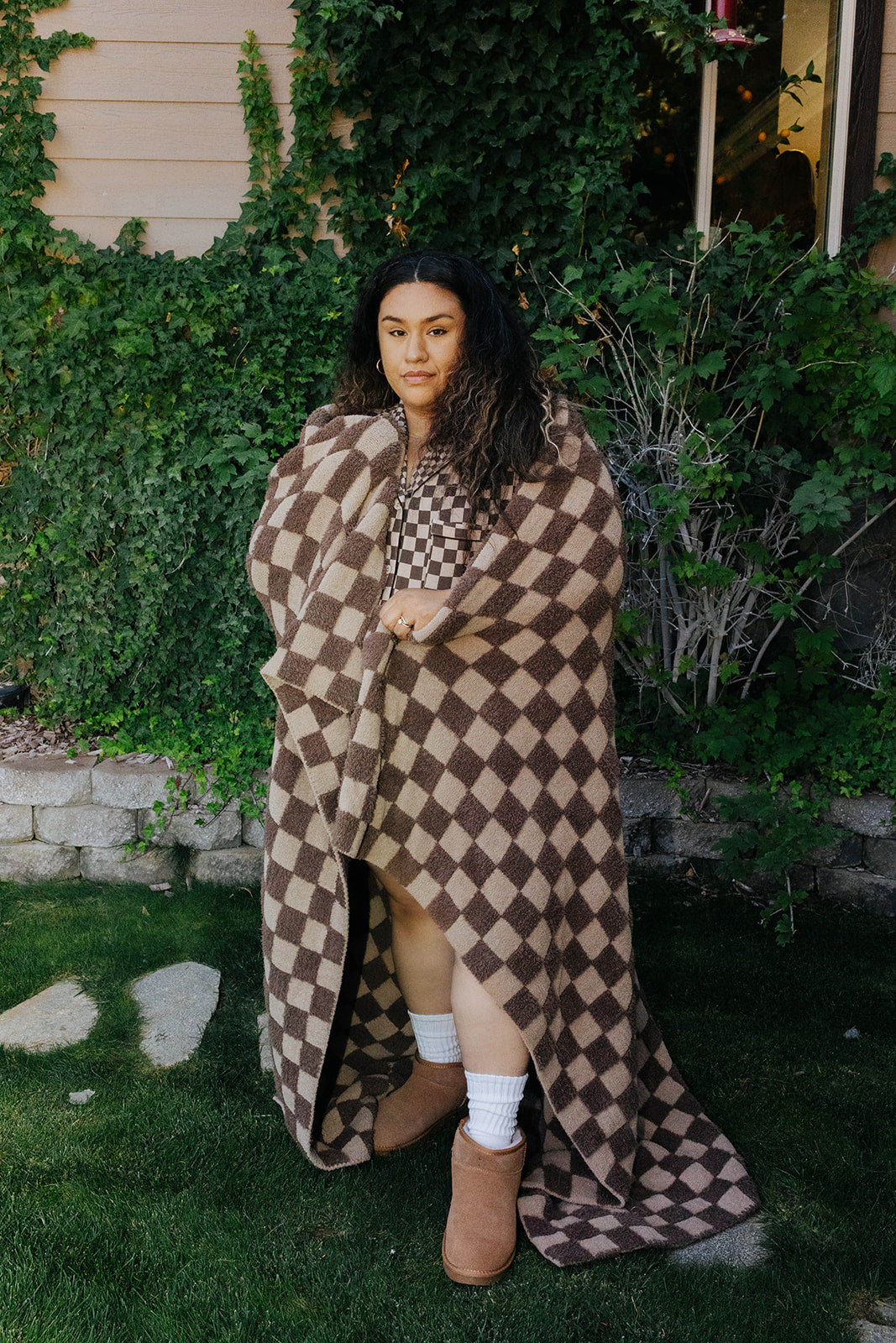Model holding the tonal brown check blanket open outdoors to show its full size.