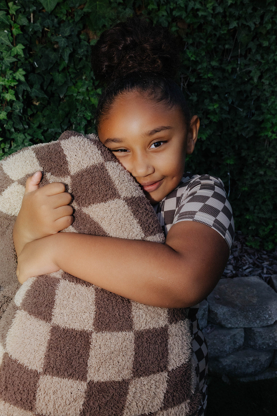 Child holding a tonal brown check quillow folded into a pillow.