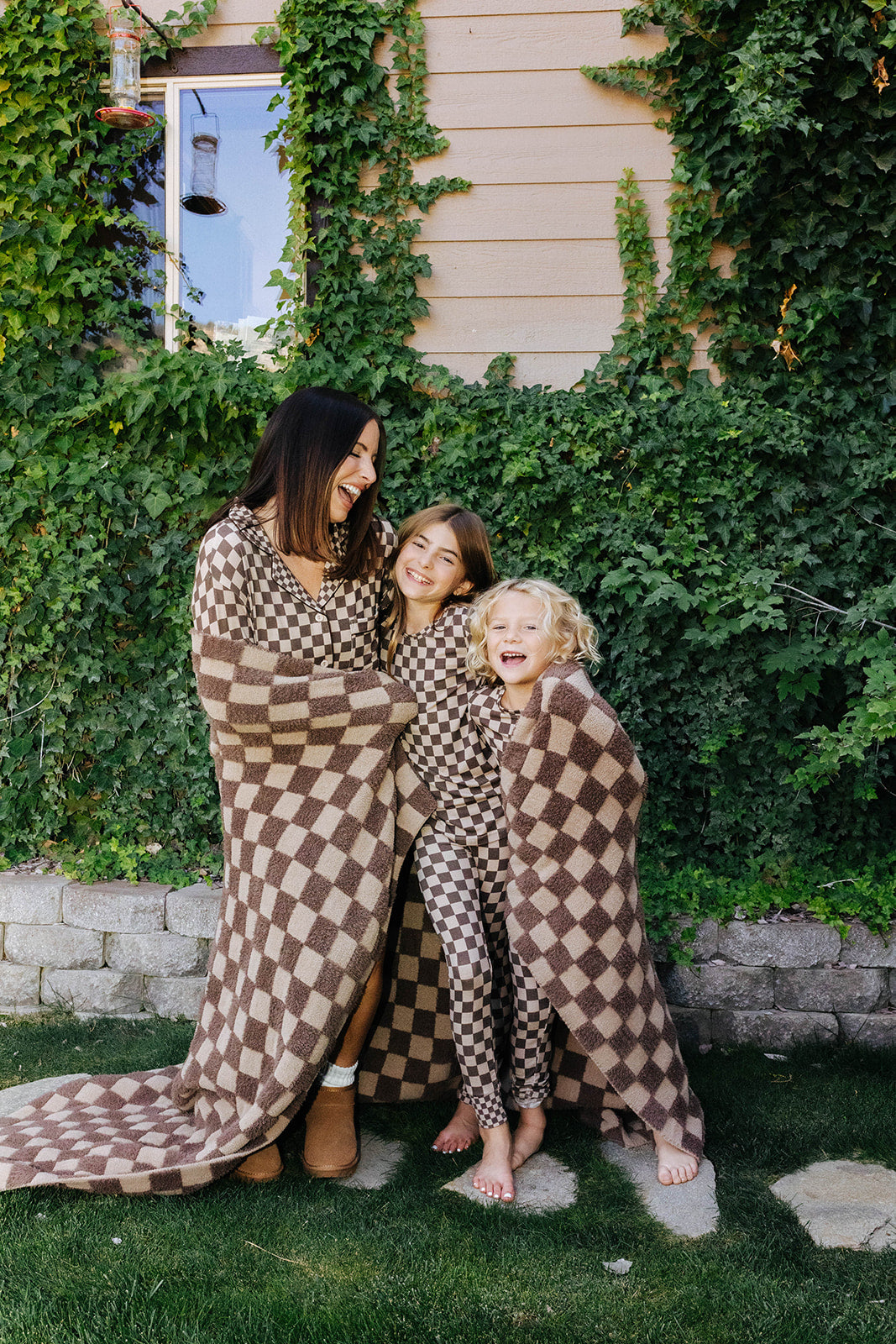 Adult and two children wearing matching brown check pajamas outdoors.