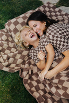 Adult and children in matching brown check pajamas lying on a tonal brown check blanket.