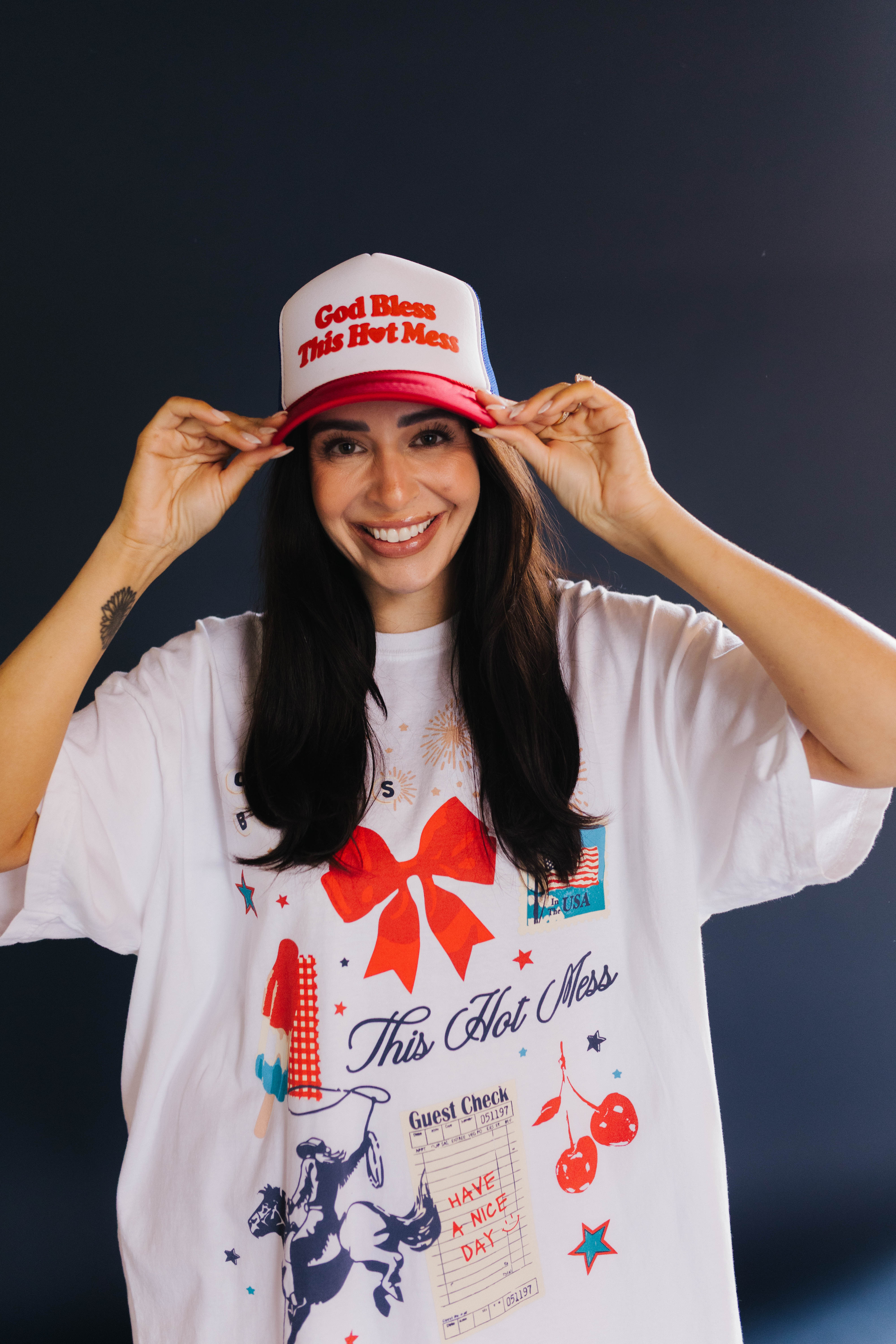 person smiling showing the front of the hat that says god bless this hot mess