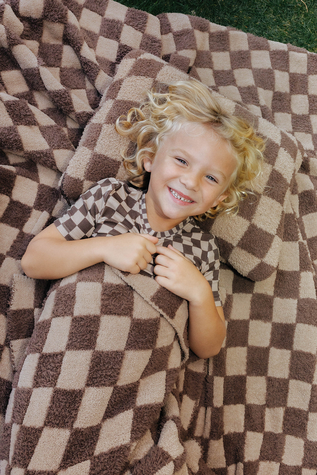 Child smiling on the brown check kids blanket outdoors.