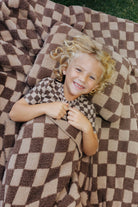 Child smiling on the brown check kids blanket outdoors.