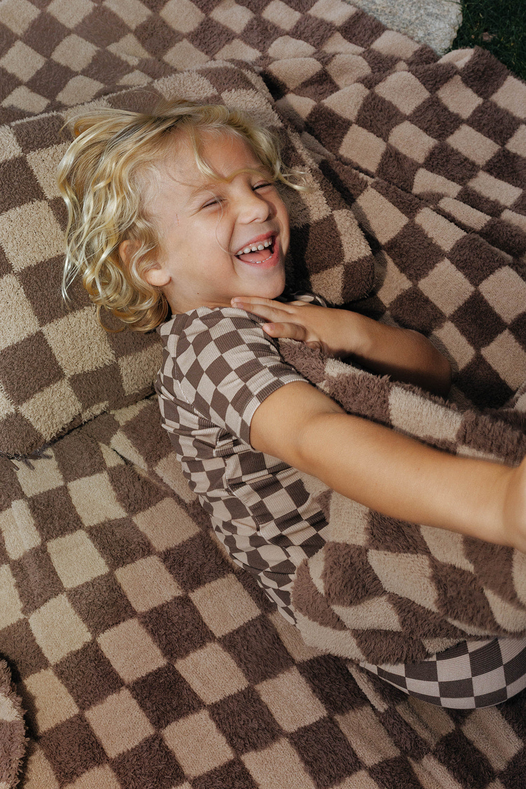 Child lying on the brown check blanket, showing the two tone checkerboard pattern.