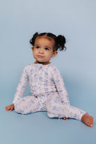 Child wearing a light blue romper with floral patterns on a solid background