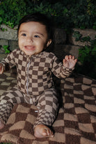 Baby wearing the brown check zip pajamas while seated on a blanket.