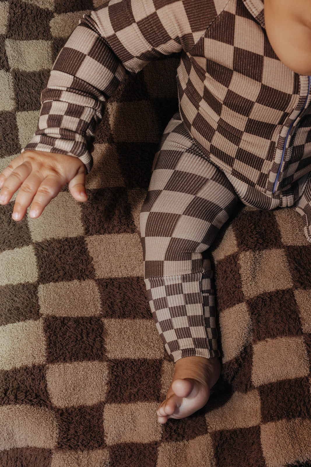 Close view of a baby wearing brown check zip pajamas on a tonal brown check kid blanket.