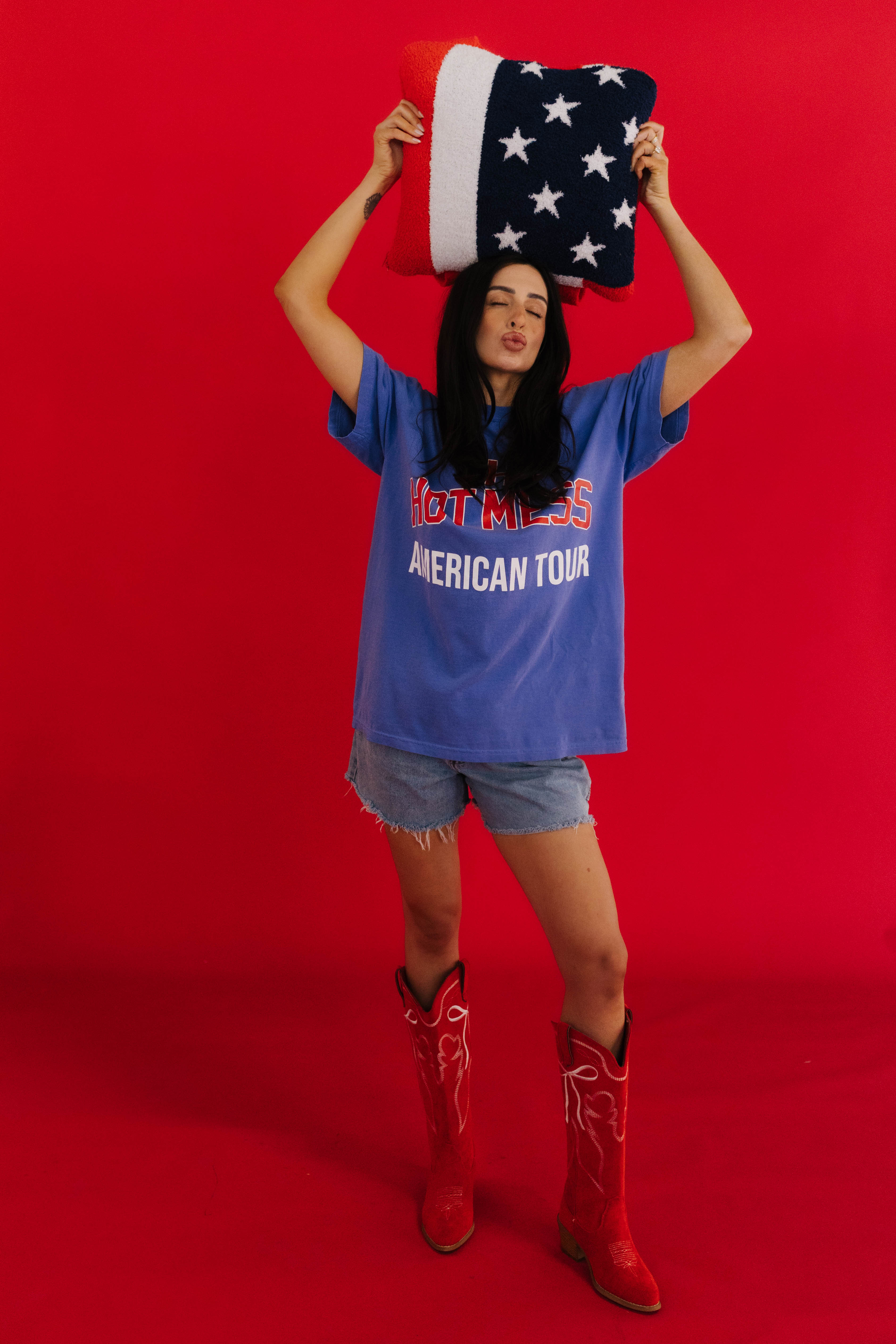 Person wearing a blue t-shirt with text and denim shorts, holding an American flag quillow 