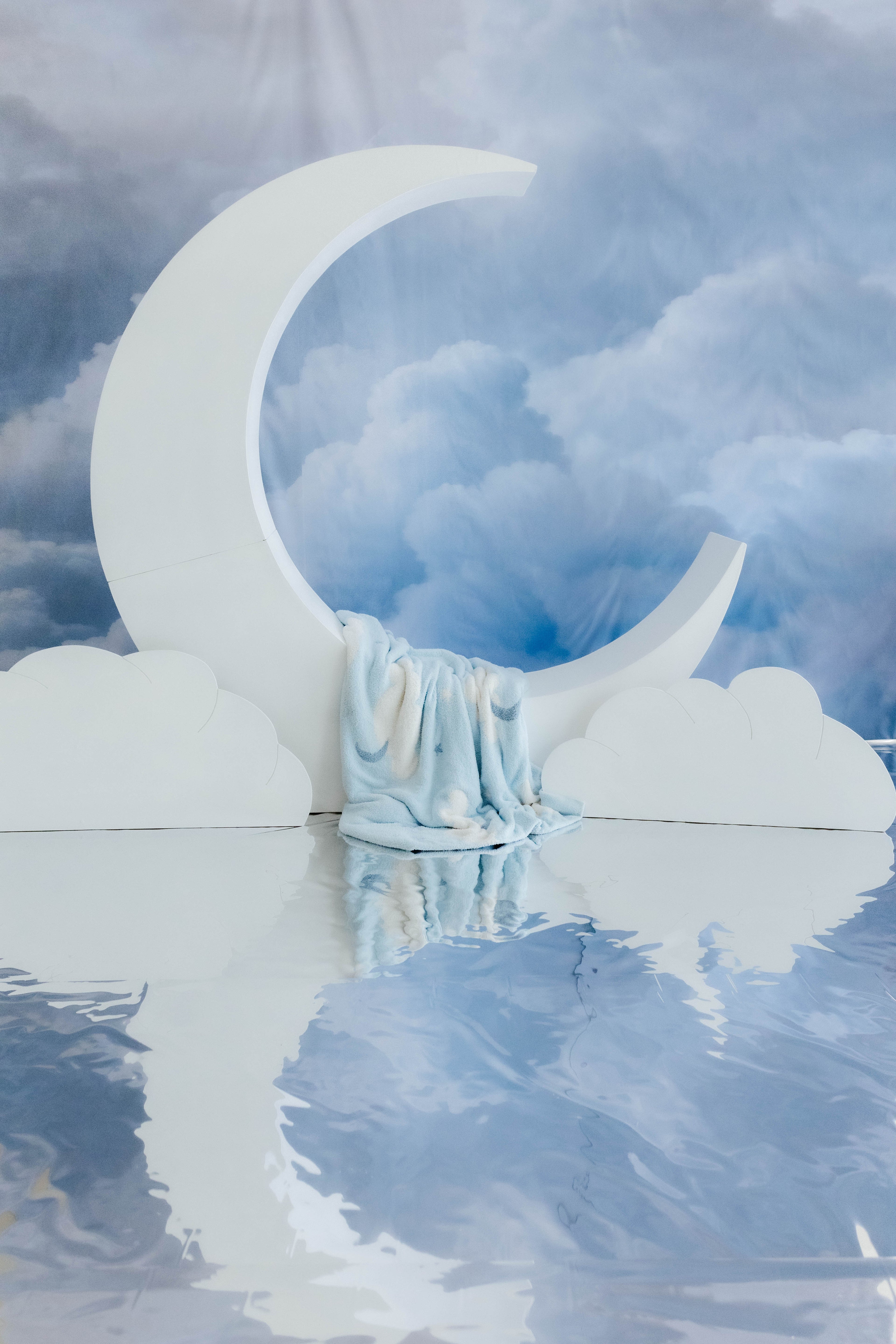 cloud baby blanket laying on moon decoration with cloud decorations in the back 
