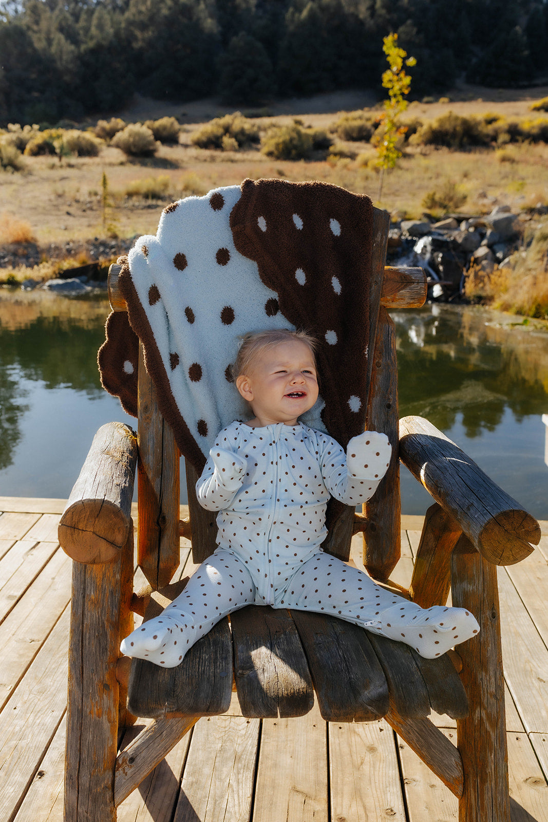 Full length front view of baby blue and brown polka dot zip pajamas, with hands and feet visible.