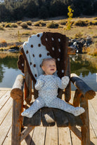 Full length front view of baby blue and brown polka dot zip pajamas, with hands and feet visible.