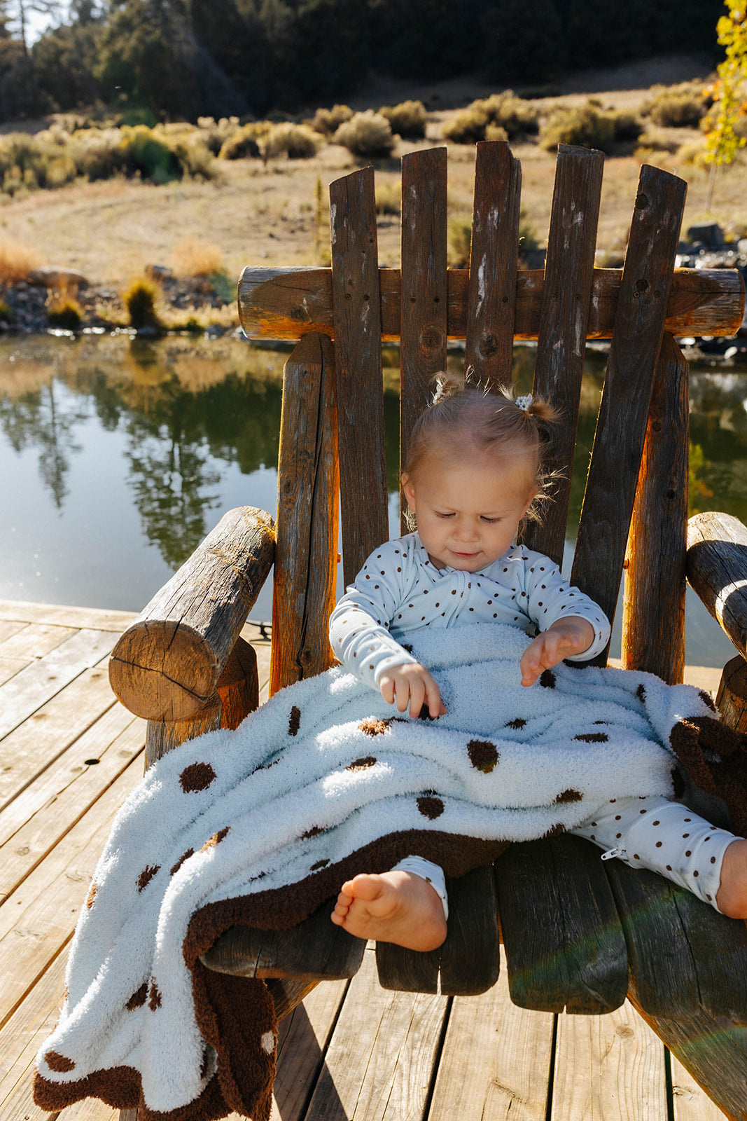 Baby wearing blue polka dot zip pajamas with the matching kid blanket across their lap.